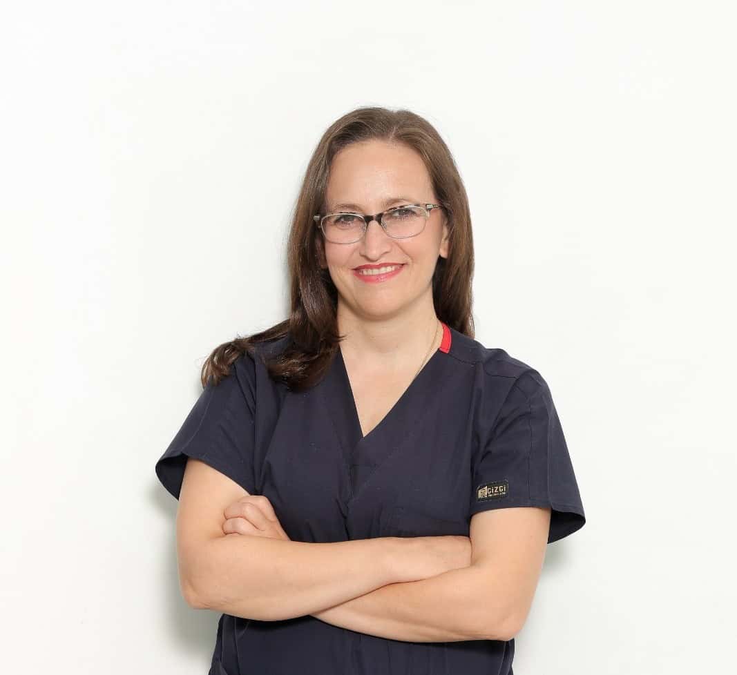 Dentiste femër me syze, duke buzëqeshur me vetëbesim në një klinikë dentare.