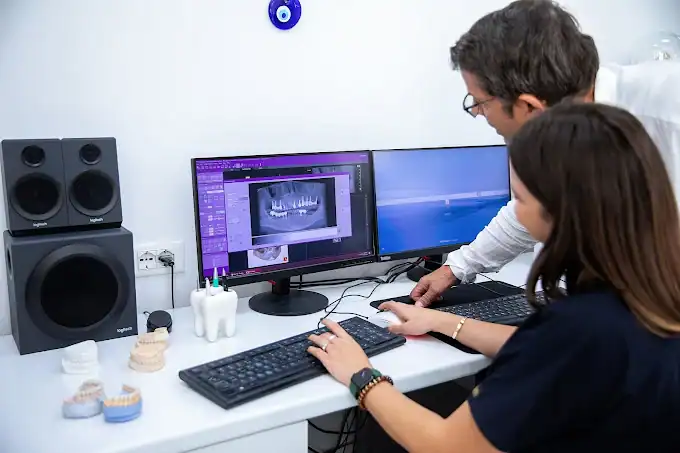 Dentista e paziente che esaminano immagini radiografiche dentali digitali su schermi di computer.