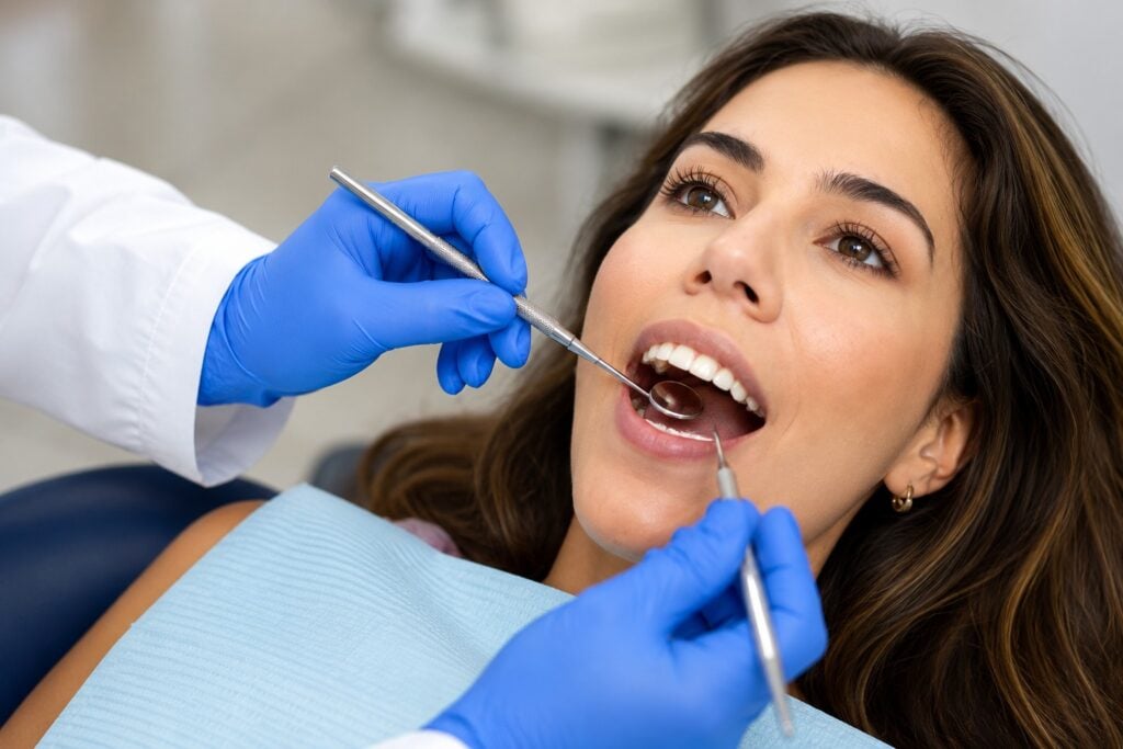Woman receiving dental examination at dental clinic with dentist using mirror and probe.